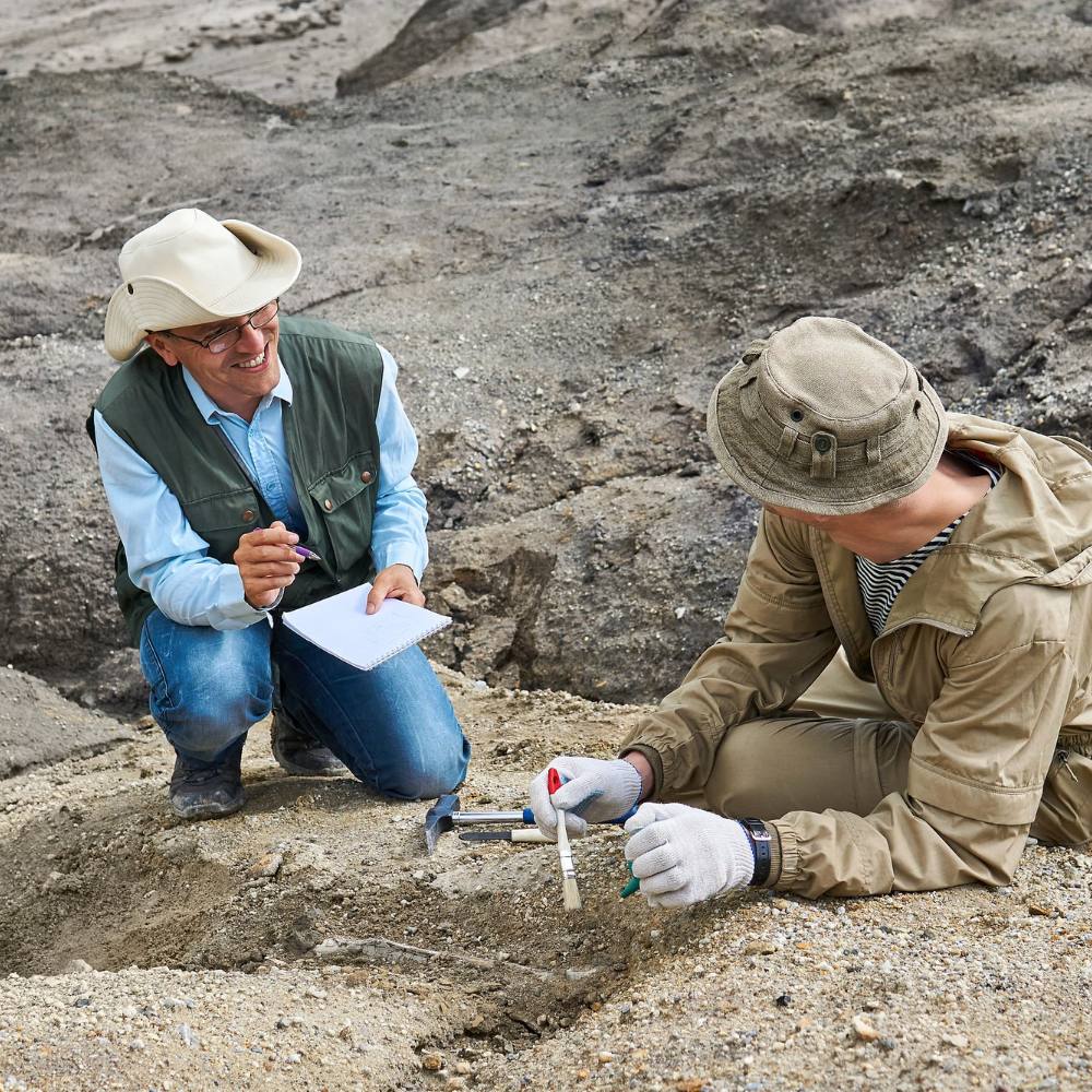 Geologist in a helmet beats a rock with a hammer to take a sample of the mineral