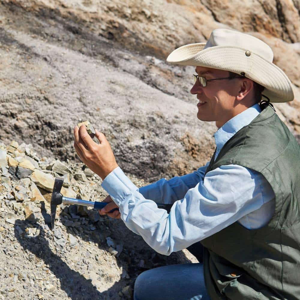 Man geologist in a desert area examines a rock sample against the backdrop of a colored